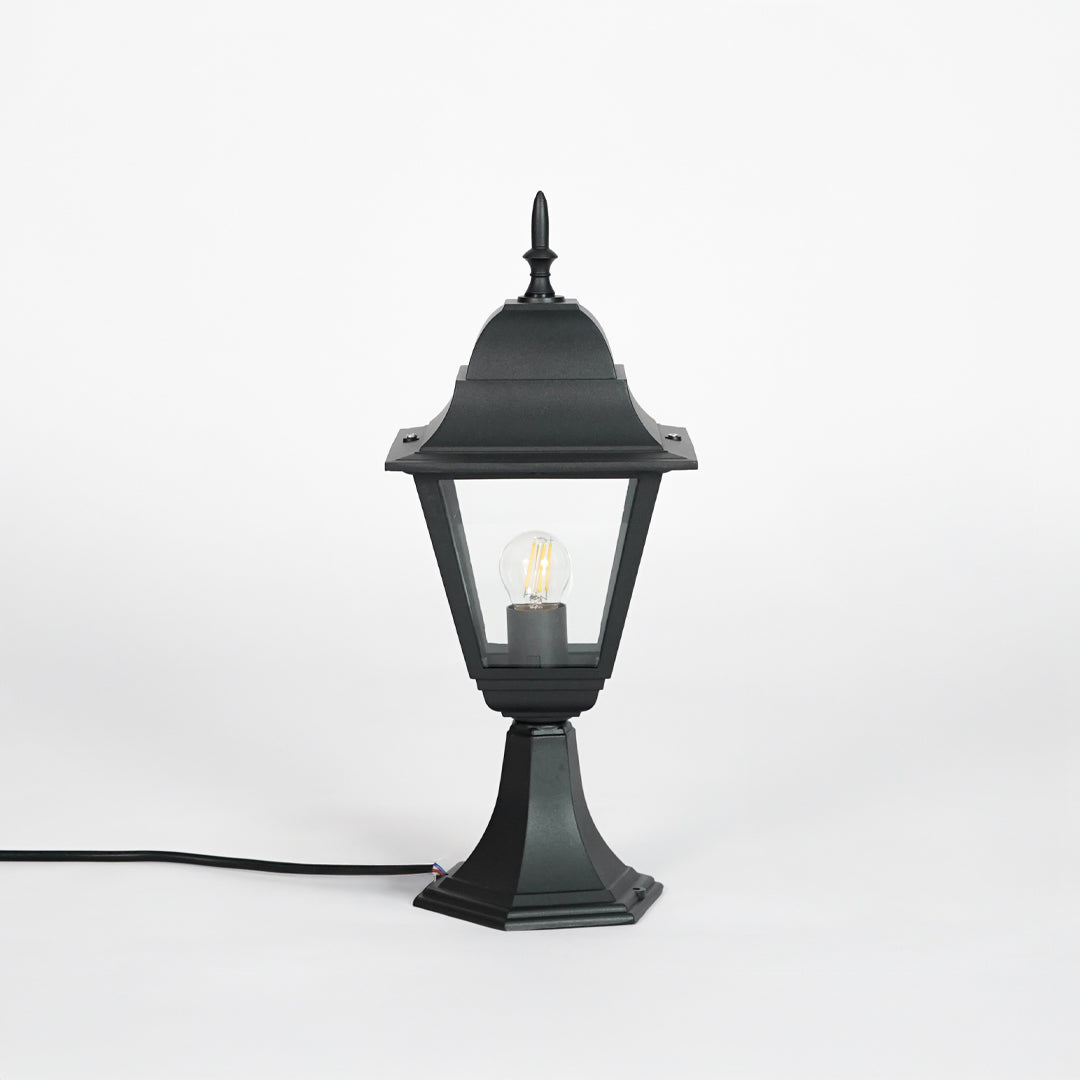 Background: Black outdoor gate light with glowing bulb and clear glass shade for modern exterior decor use.