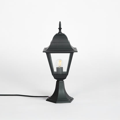 Background: Black outdoor gate light with glowing bulb and clear glass shade for modern exterior decor use.
