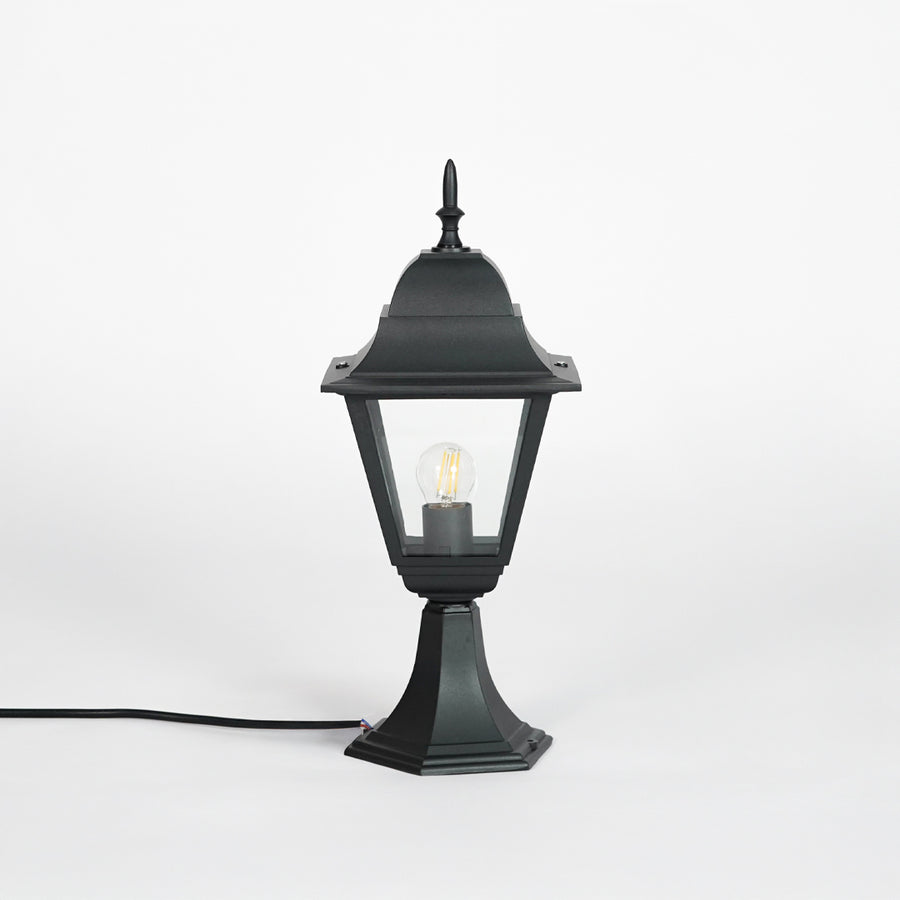 Background: Black outdoor gate light with glowing bulb and clear glass shade for modern exterior decor use.