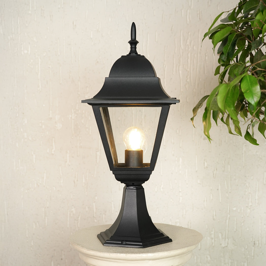 Modern black outdoor gate light with warm glow styled beside plants for elegant exterior decor ambiance.