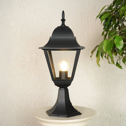Modern black outdoor gate light with warm glow styled beside plants for elegant exterior decor ambiance.