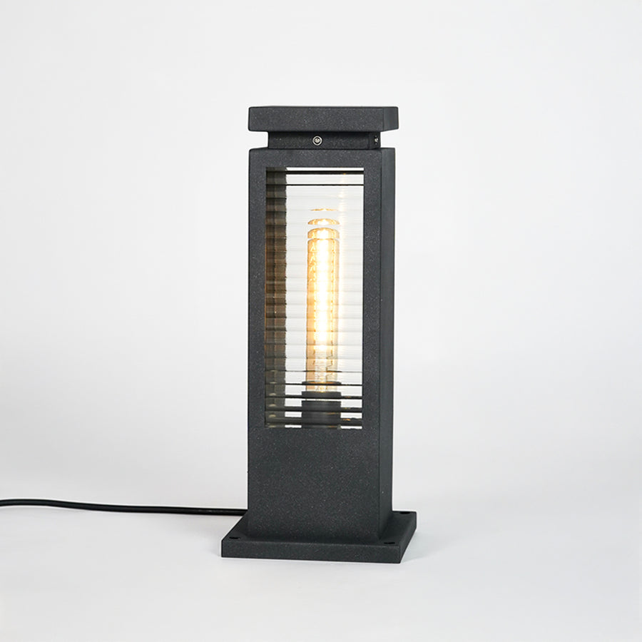 Black metal outdoor bollard light with clear glass panels for modern exterior lighting decor placement styling.