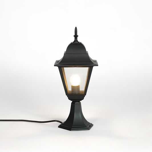 Black outdoor gate light with warm glowing bulb and clear glass shade for elegant exterior decor use.