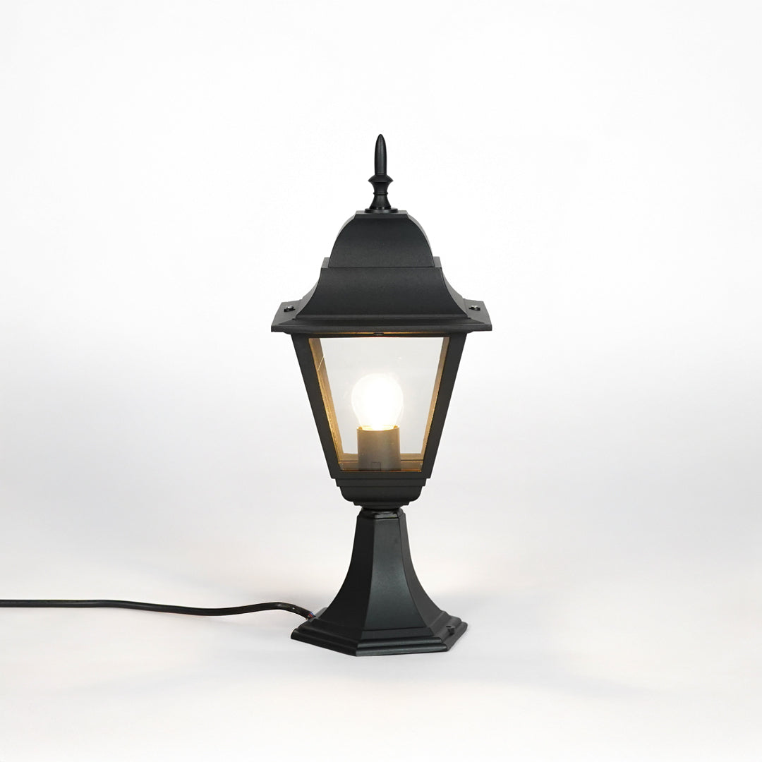 Black outdoor gate light with warm glowing bulb and clear glass shade for elegant exterior decor use.