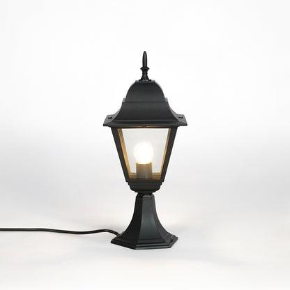 Black outdoor gate light with warm glowing bulb and clear glass shade for elegant exterior decor use.