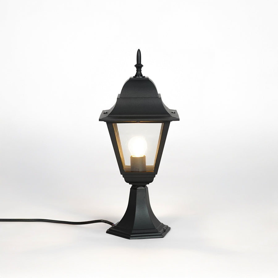Black outdoor gate light with warm glowing bulb and clear glass shade for elegant exterior decor use.