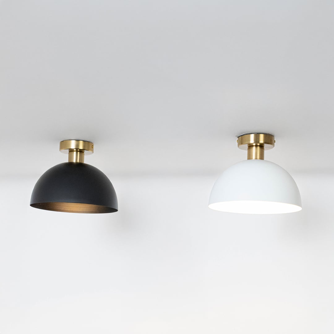 Black and white ceiling lights with gold fittings and dome shades glowing on white background for modern home lighting.
