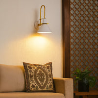 White and gold wall sconce glowing warmly beside bed adding modern elegance and charm to cozy home interiors.