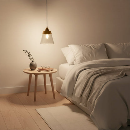 Gold metal and clear glass cone pendant light glowing warmly beside a cozy bed creating soft ambient bedroom lighting and a calm modern decor vibe.