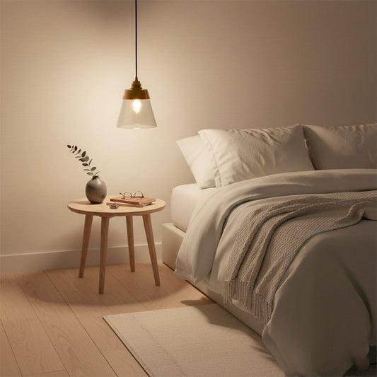 Gold metal and clear glass cone pendant light glowing warmly beside a cozy bed creating soft ambient bedroom lighting and a calm modern decor vibe.