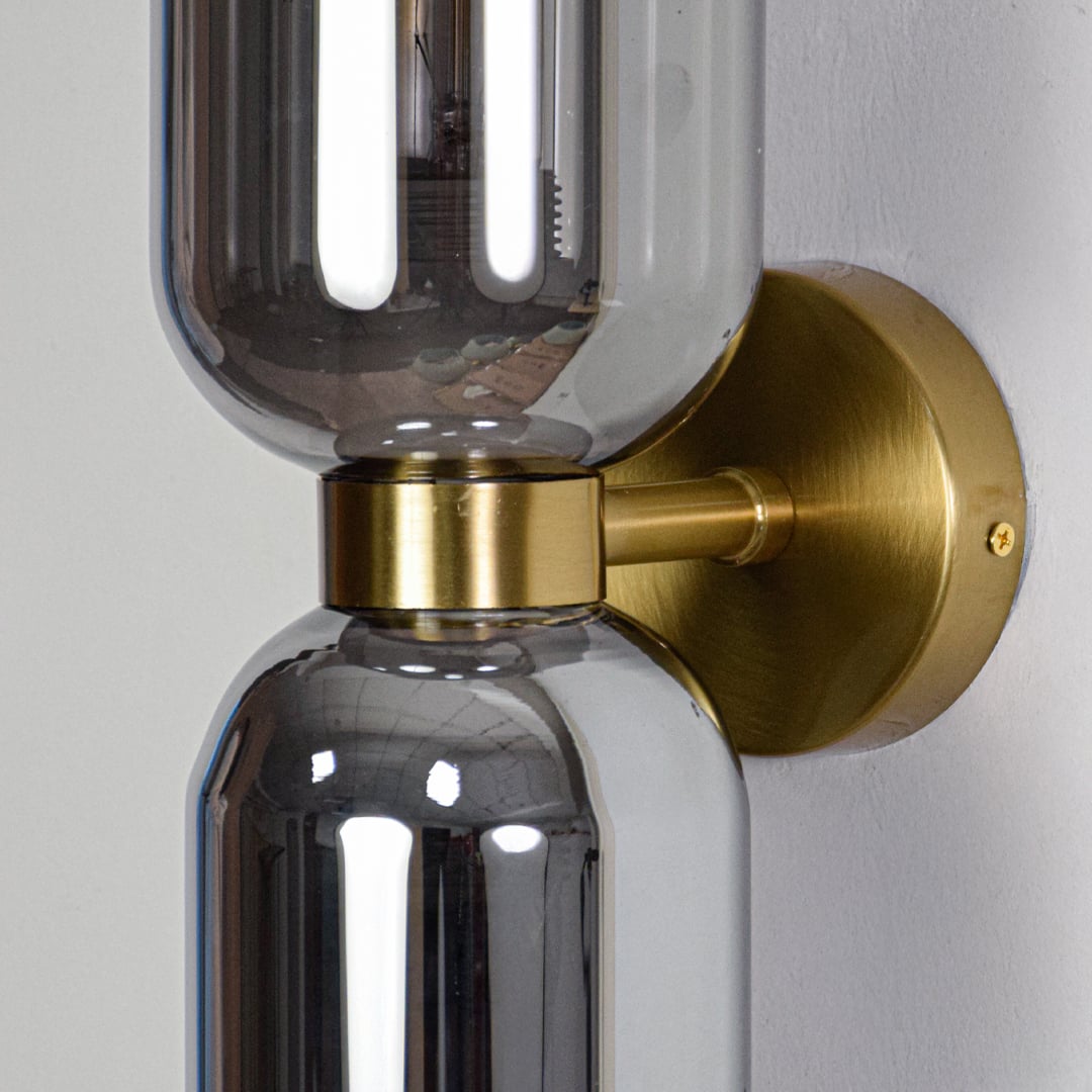 Close view of gold metal holder and dual smoked glass cylinders for premium wall lighting design.
