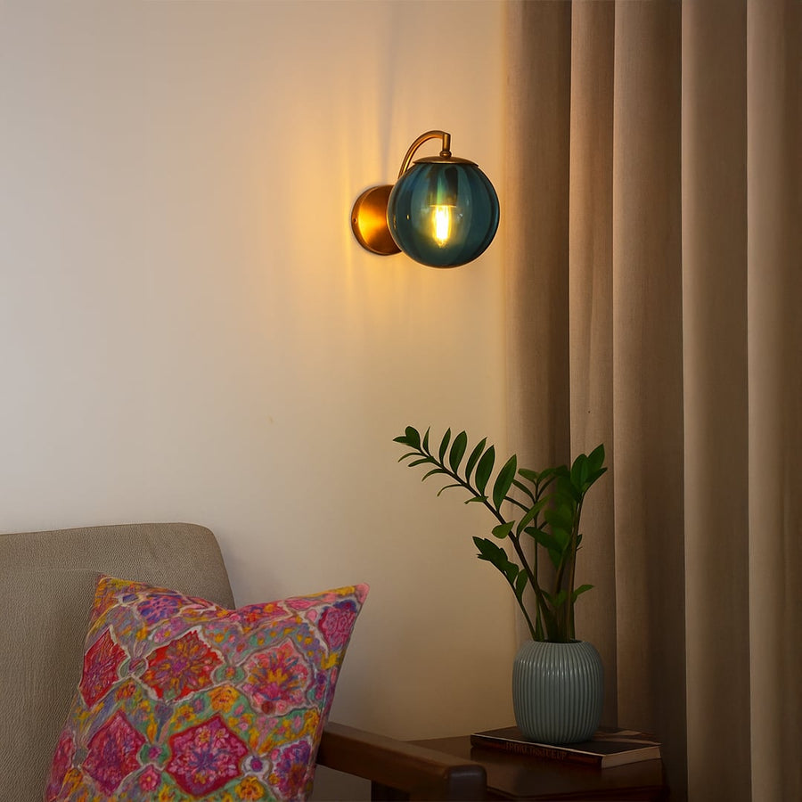 Blue glass globe wall light with gold metal base glowing warmly beside bed adding elegance to modern interiors.