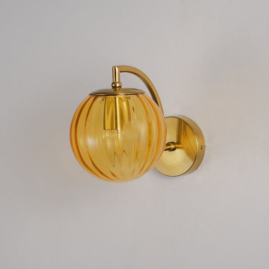 Brass wall light with round amber glass globe shade displayed against plain white wall backdrop.