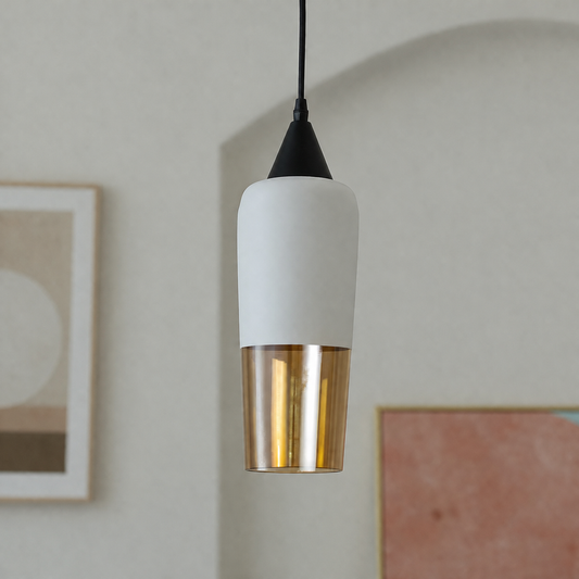 A modern pendant light with a matte white cylindrical shade and a brushed gold metallic lower section, suspended by a black cord against a softly blurred interior wall.