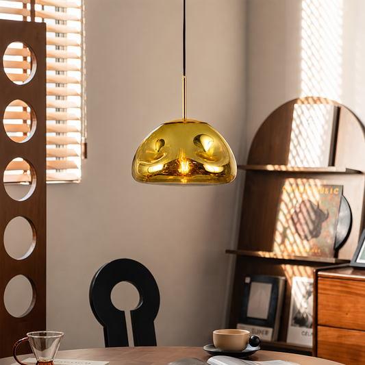 A modern pendant light with a glossy, wavy gold glass dome shade hanging over a dining table in a stylishly decorated room.