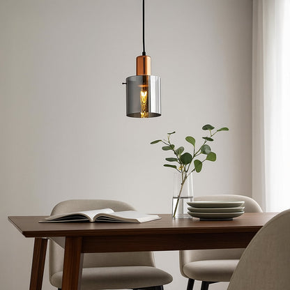 A modern copper and smoky glass pendant light glowing warmly above a wooden dining table creating soft ambient lighting for clean contemporary home decor.