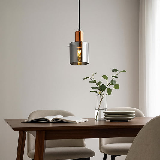 A modern copper and smoky glass pendant light glowing warmly above a wooden dining table creating soft ambient lighting for clean contemporary home decor.