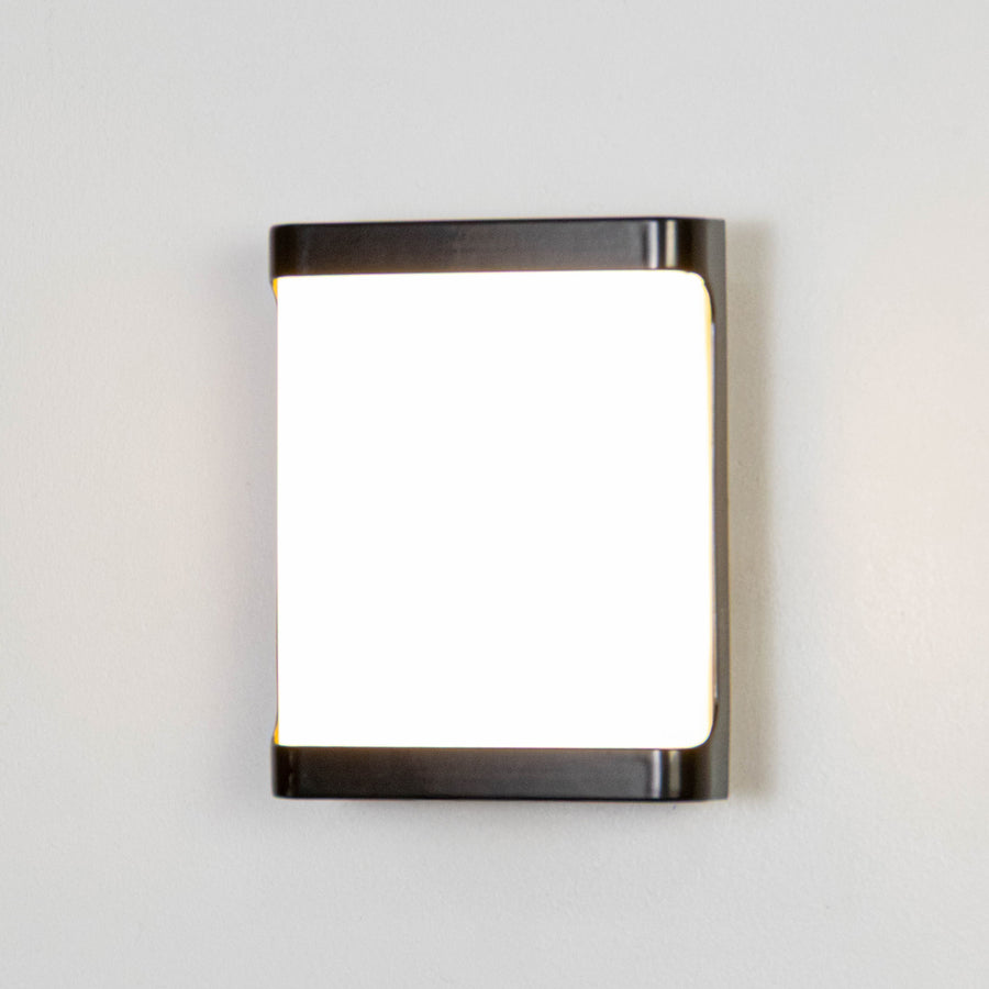 Black metal wall light on white background with frosted glass shade for minimalist modern decor.