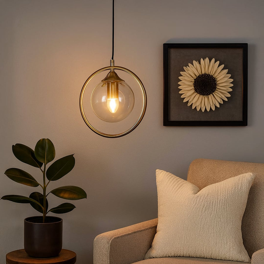 A warm pendant light with a clear glass globe and gold ring frame glows softly in a cozy living room beside a cushioned armchair and wall art creating a calm ambient setting.