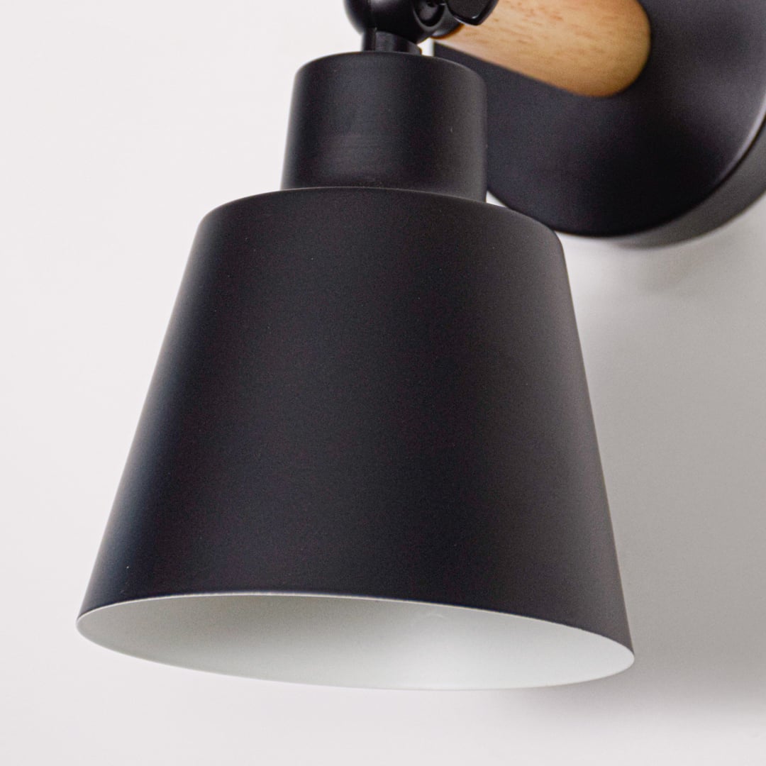 Black metal wall light closeup showing matte finish shade and curved arm detail designed for modern minimalist interior lighting.