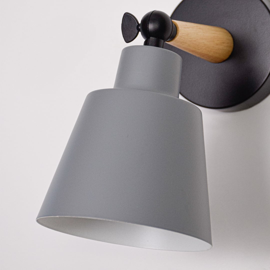 Closeup of grey metal wall light shade showing smooth finish wooden arm connection and solid black metal mounting plate.