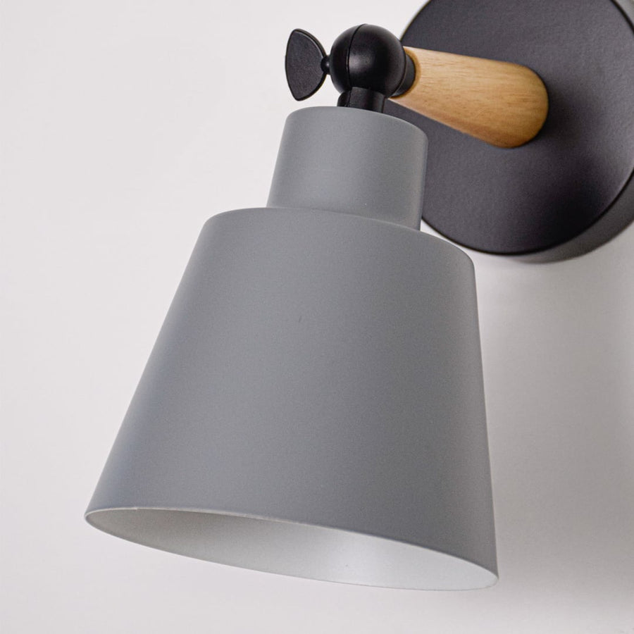 Closeup of grey metal wall light shade showing smooth finish wooden arm connection and solid black metal mounting plate.