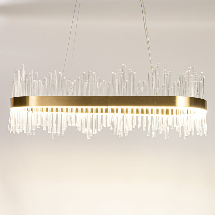 Gold metal chandelier with clear glass rods shown with lights on against a white background highlighting its bright elegant illumination.