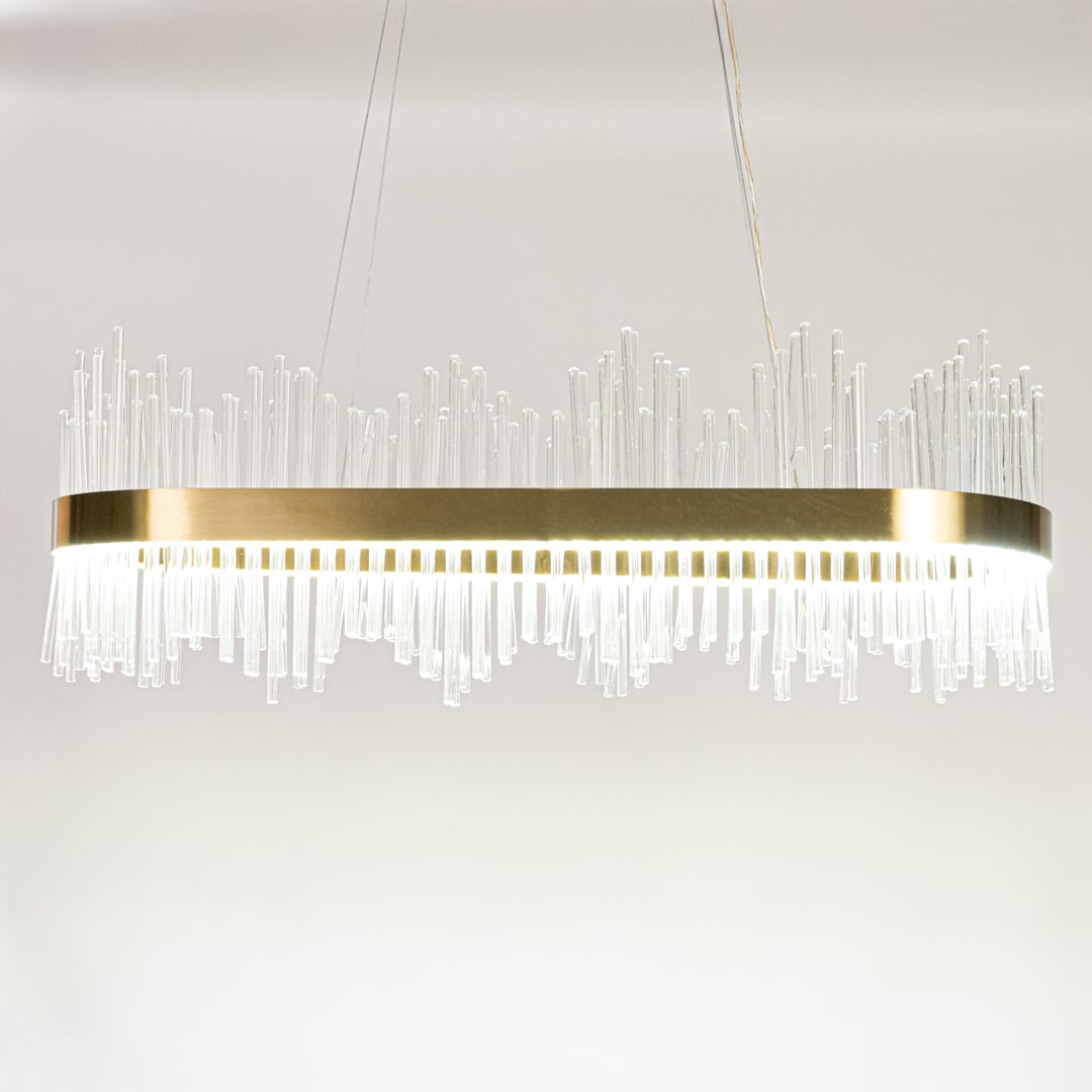 Gold metal chandelier with layered glass rods shown with lights on against a white background emphasizing its warm glowing upscale design.