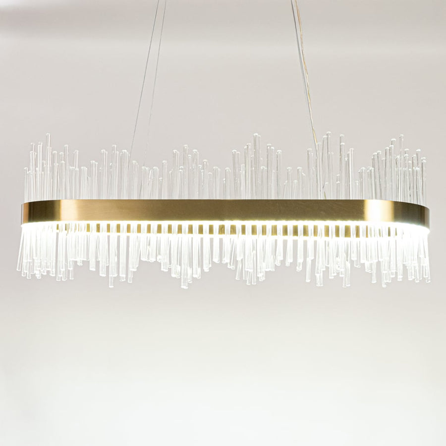 Gold metal chandelier with layered glass rods shown with lights on against a white background emphasizing its warm glowing upscale design.