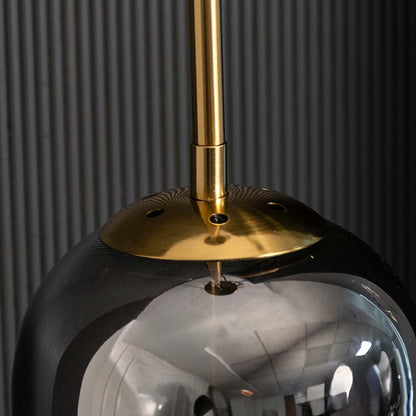 Closeup of smoked grey cylindrical glass pendant with gold fitting and warm mesh diffuser showcasing its refined modern craftsmanship.