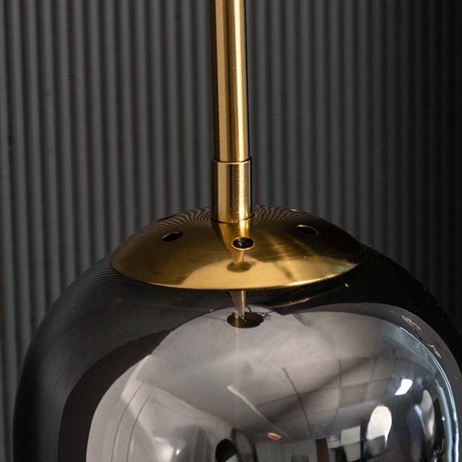 Closeup of smoked grey cylindrical glass pendant with gold fitting and warm mesh diffuser showcasing its refined modern craftsmanship.