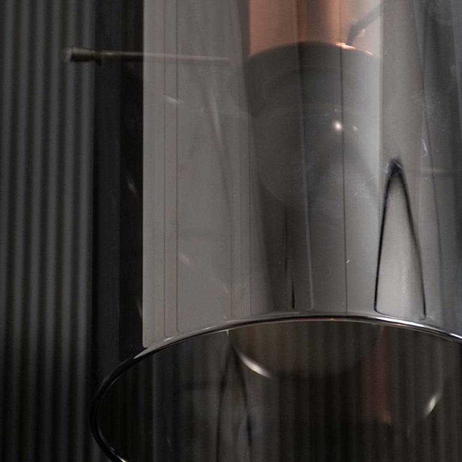 A closeup view of the copper and smoky glass pendant light highlighting its warm illuminated filament bulb and refined metallic finish.