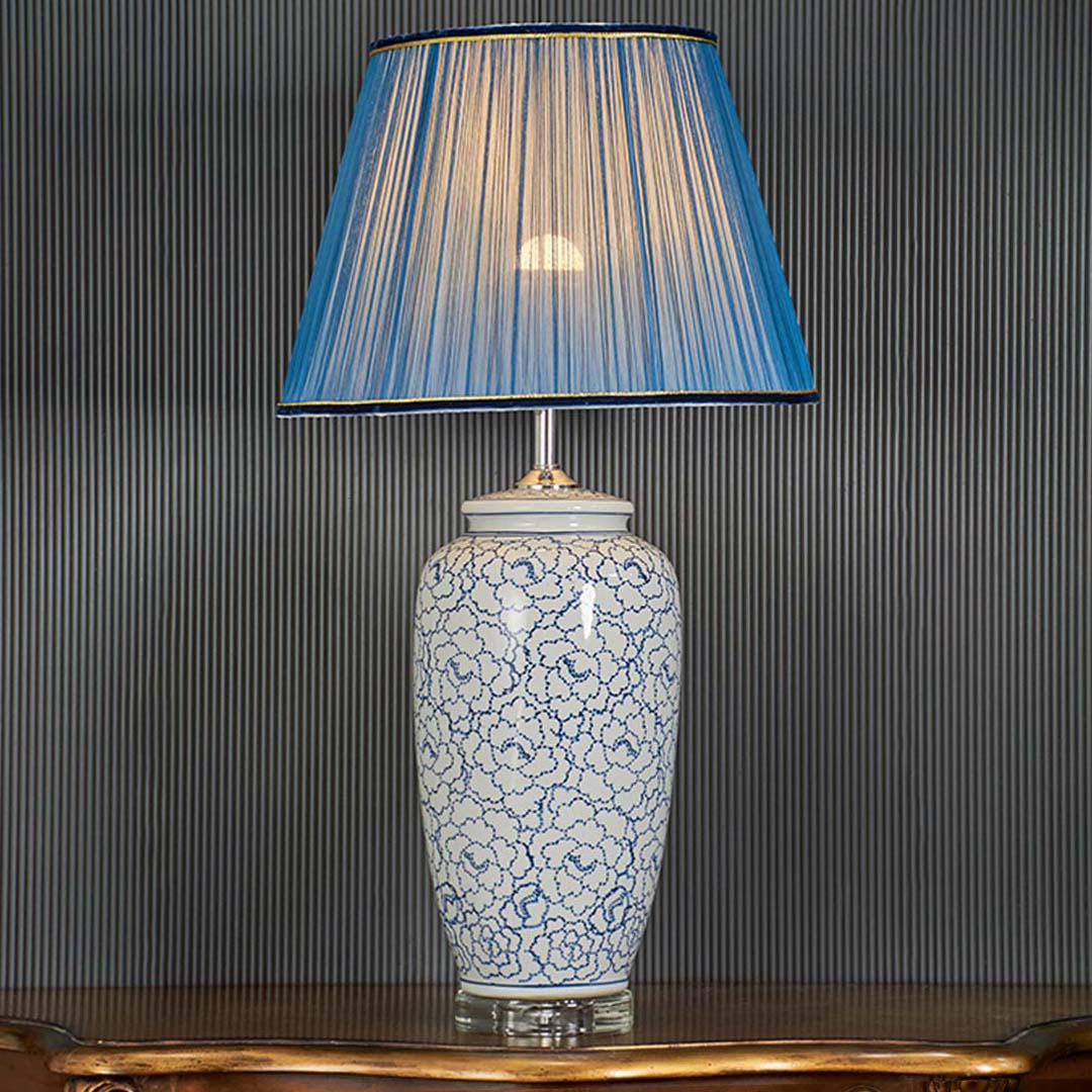 Blue floral ceramic table lamp illuminated against a black background creating a striking contrast that highlights its intricate floral artwork.