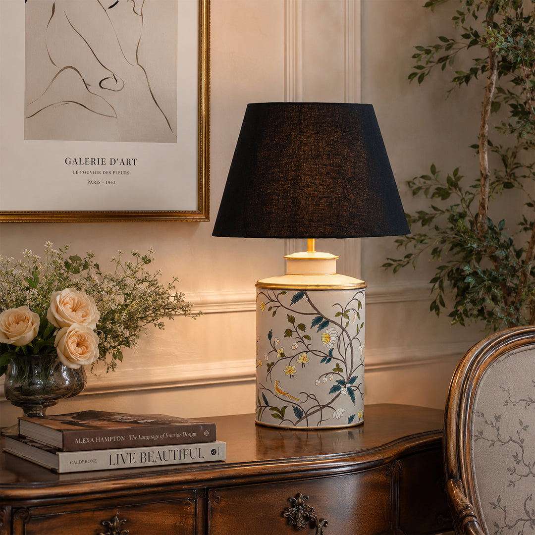 Floral ceramic table lamp with black fabric shade creating warm ambient lighting in an elegant living room setting.