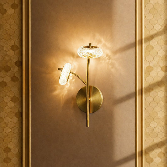 Gold metal wall light with crystal glass shade casting warm glow ideal for bedroom or hallway wall decor in elegant interior setting.