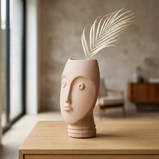 Peach ceramic face vase with dried palm leaf placed on wooden table for stylish home decor styling.