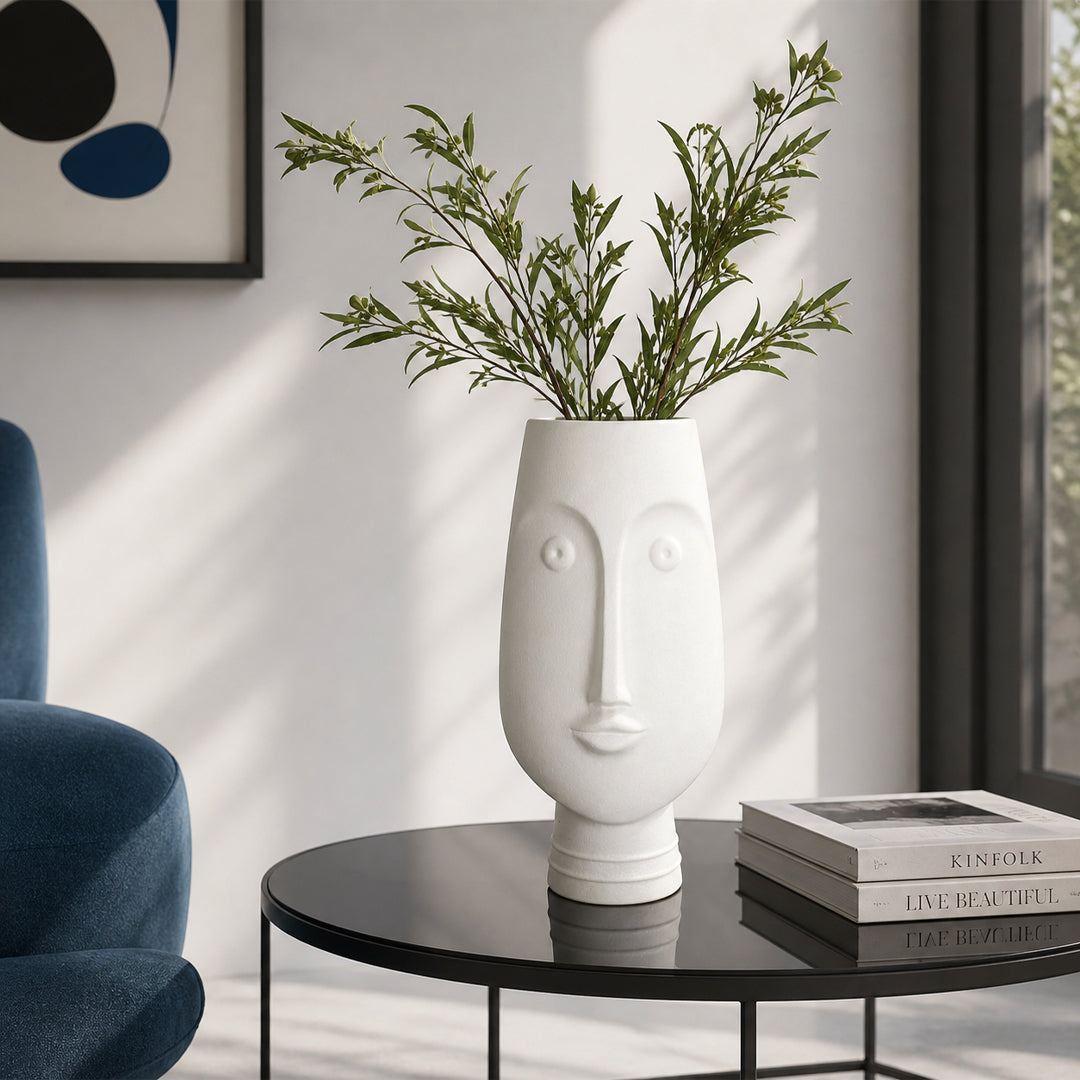 White ceramic face flower vase with green stems placed on side table for modern home decor styling.