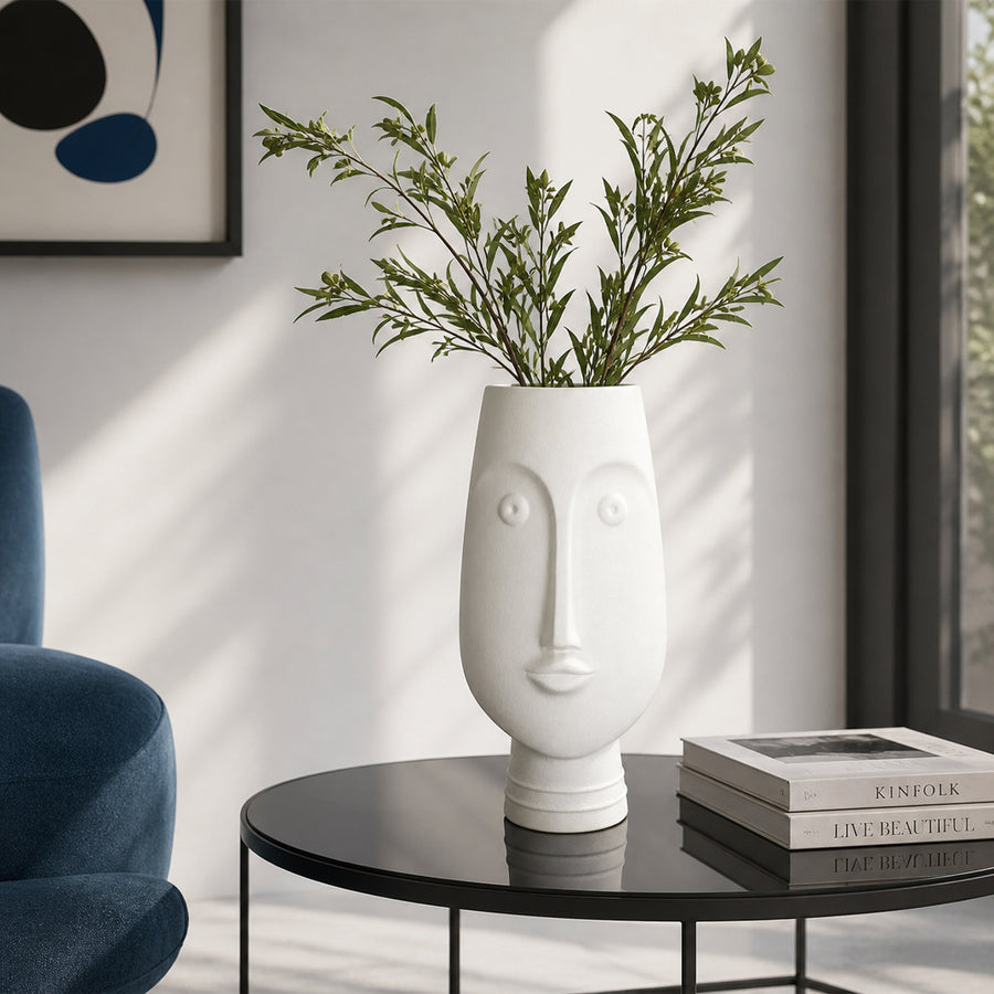 White ceramic face flower vase with green stems placed on side table for modern home decor styling.