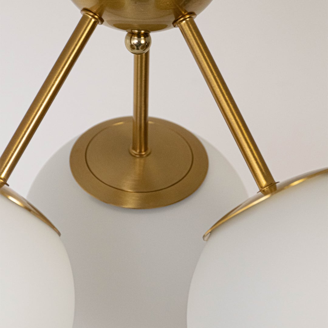 Closeup of gold ceiling light with three frosted glass globes on sleek frame for modern home lighting and ceiling decor.