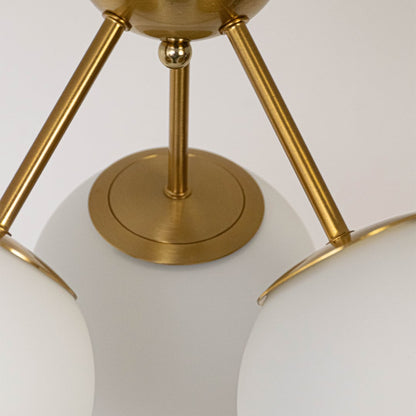 Closeup of gold ceiling light with three frosted glass globes on sleek frame for modern home lighting and ceiling decor.