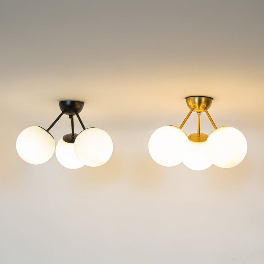 Black and gold ceiling lights with triple frosted glass globes glowing on white background for stylish home ceiling decor.