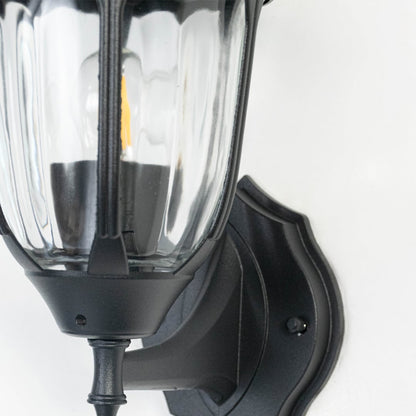 Closeup image of black metal outdoor wall light with ribbed glass shade for stylish patio lighting decor.