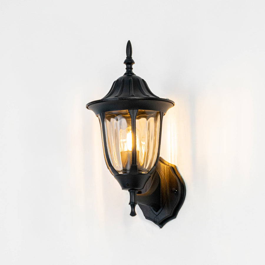 Black metal outdoor wall light on white background with clear ribbed glass shade for elegant exterior decor.