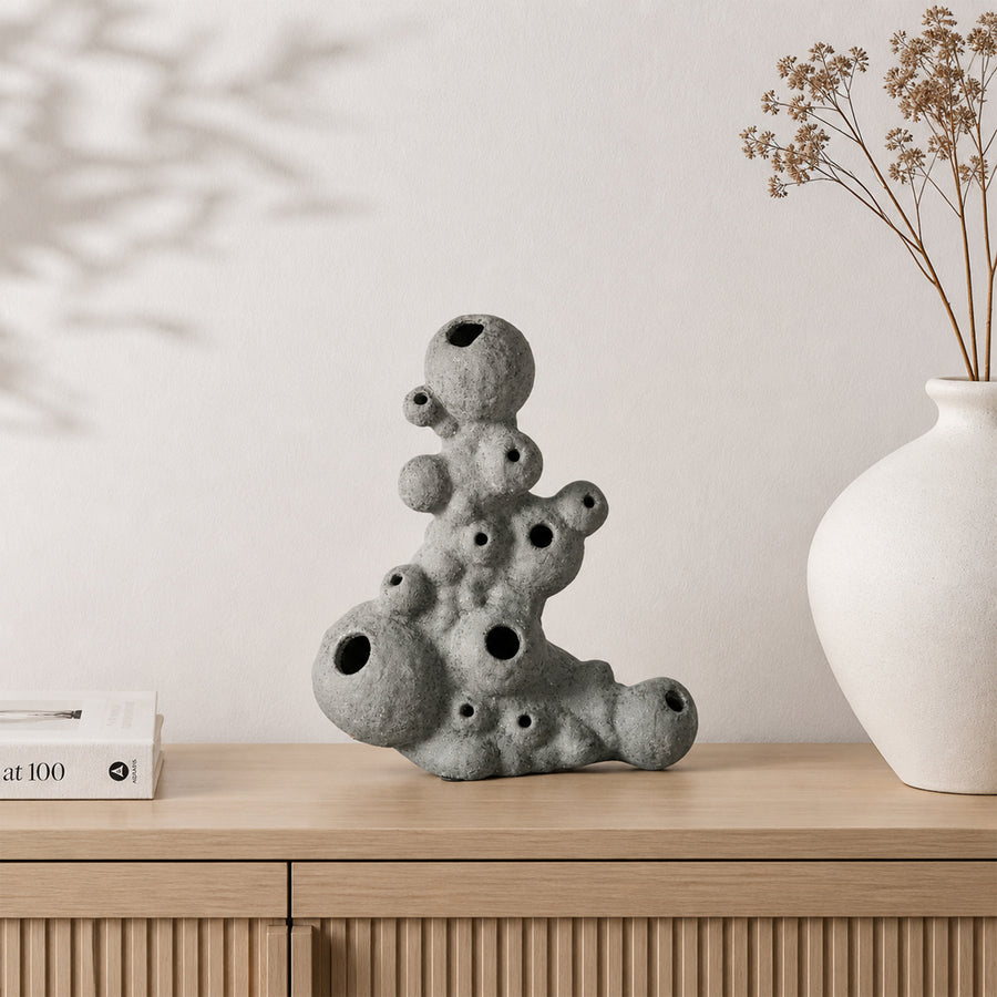 Grey abstract ceramic sculpture placed on wooden shelf with dried flowers for modern home decor styling.