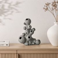 Grey abstract ceramic sculpture placed on wooden shelf with dried flowers for modern home decor styling.