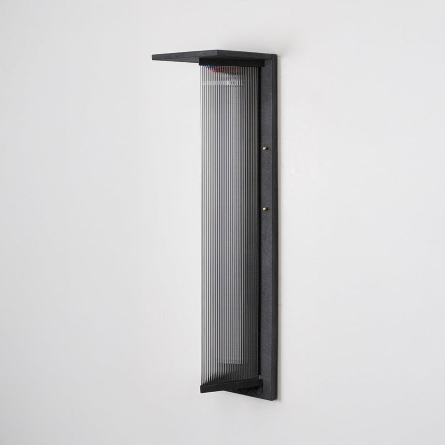 Tall modern wall light with matte black frame and ribbed glass front shown off on plain white background.