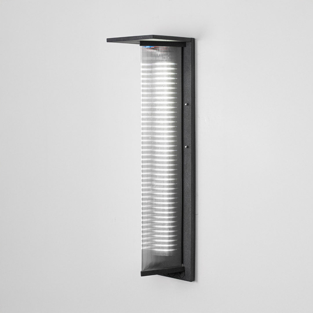 Black metal outdoor wall light on white background with ribbed glass shade for modern exterior decor.