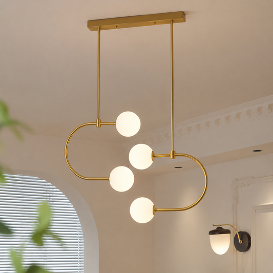 A modern gold-toned ceiling light fixture with four spherical white glass shades, suspended from a rectangular ceiling mount in a softly lit interior room.