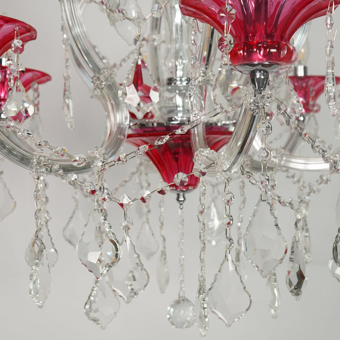 A close-up of a crystal chandelier with vibrant pink glass shades, clear faceted crystal teardrop pendants, and a silver-toned metal frame.