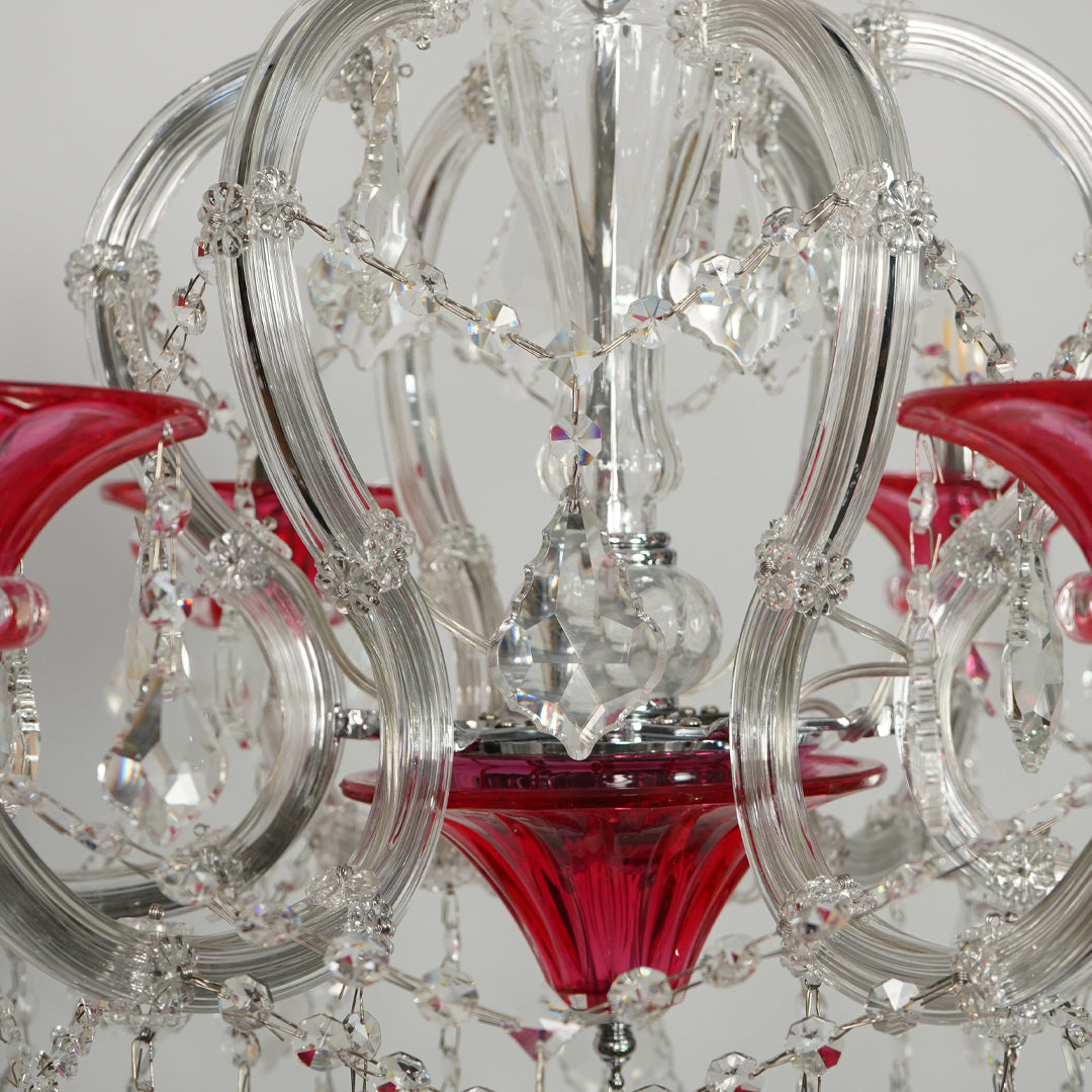 A close-up of a crystal chandelier featuring clear glass rings, hanging faceted crystal beads, and vibrant red glass shades.